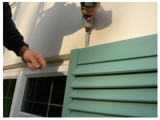 close up of drill attaching hidden bracket to top of shutter with screws