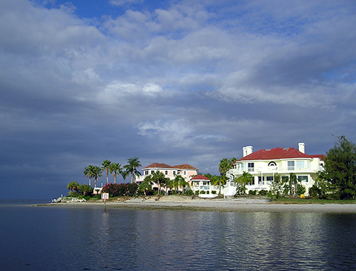 White Villa style home surrounded by palm trees and ocean 