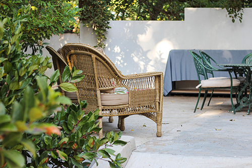 wicker chair in front of bushes in walled outdoor area 