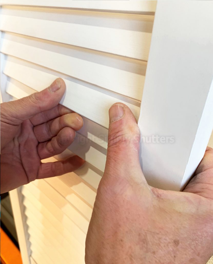 Thumbs pressing louvre blade into place on door 