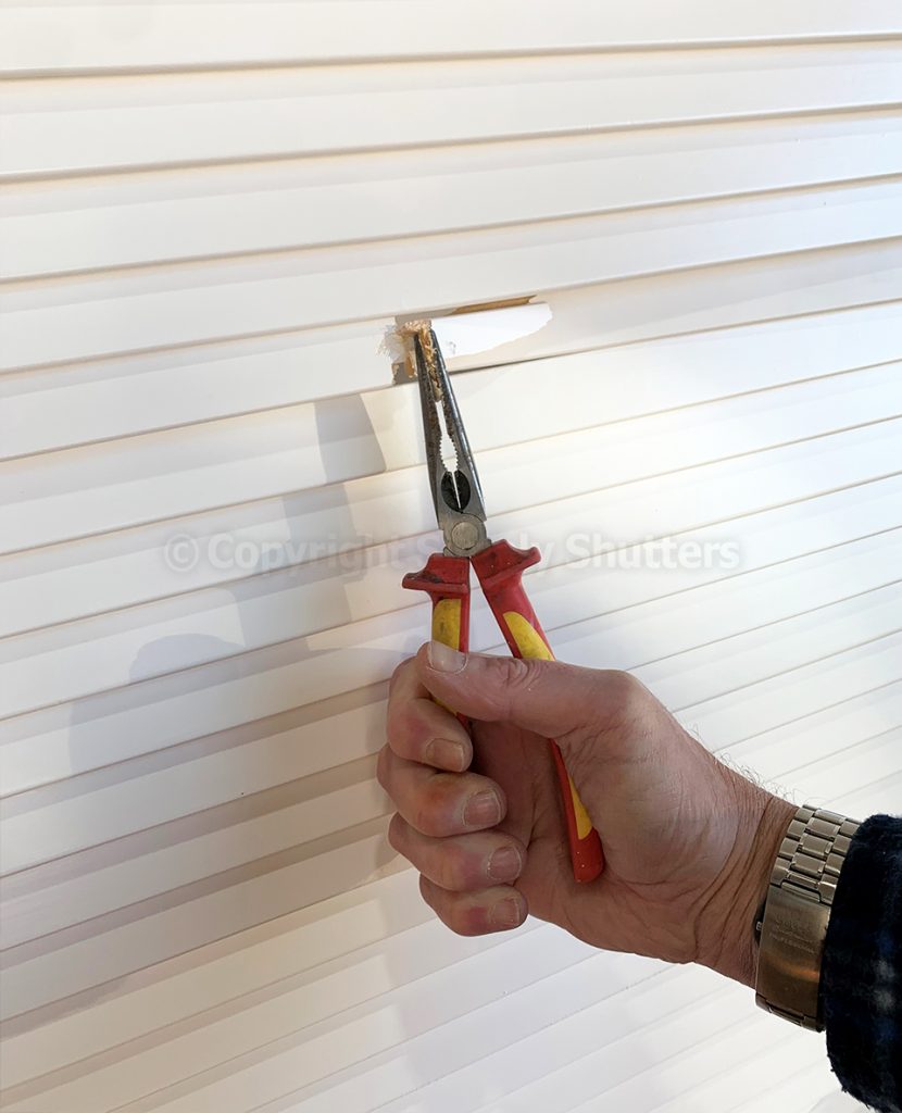 Hand holding pliers against a broken louvre blade on door 