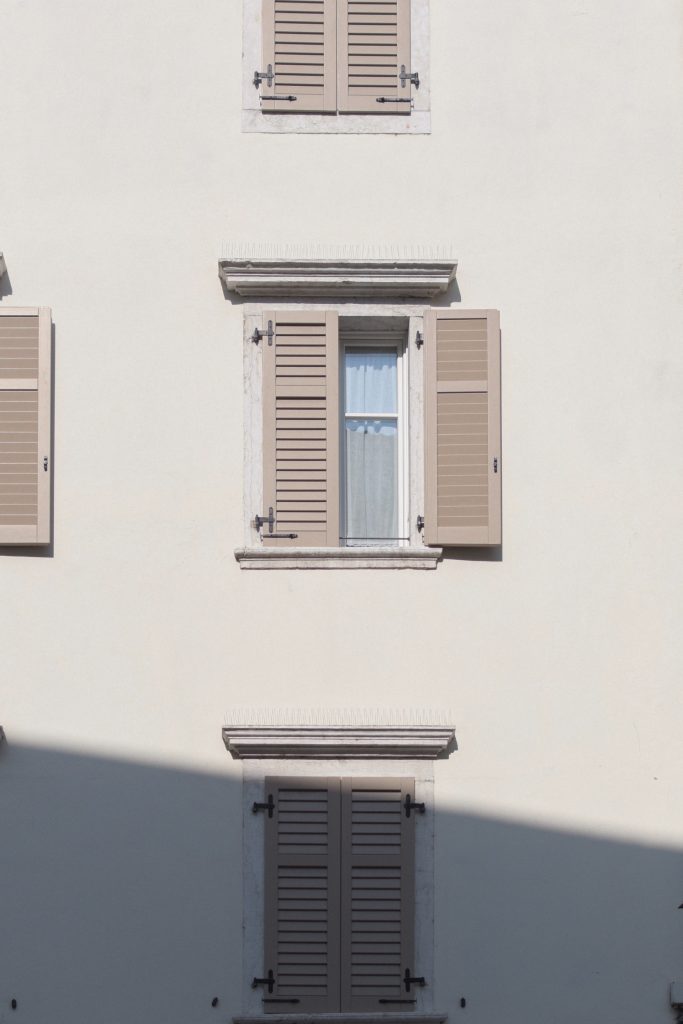 External beige shutters on a window on a building with one shutter open and the other closed. 