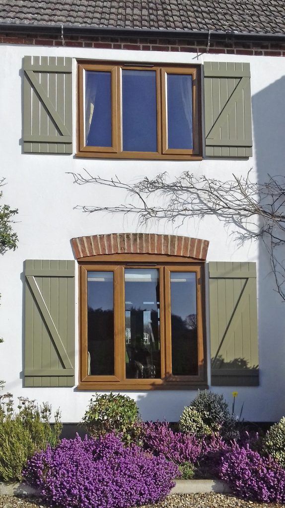 Decorative window shutters adorn a white coloured property with purple flowers under window 